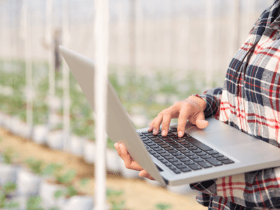 Fiatal nő laptop segítségével figyeli és elemzi a növények fejlődését egy üvegházban.